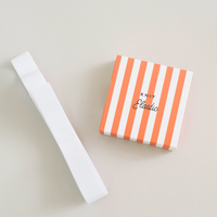 A white ribbed knit elastic band shown next to its orange and white striped packaging box with the brand name 'KNIT Elastic' printed on it, set against a neutral light beige background.