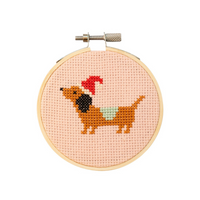 Cross-stitched dachshund with a red bow tie in a wooden hoop on a white background