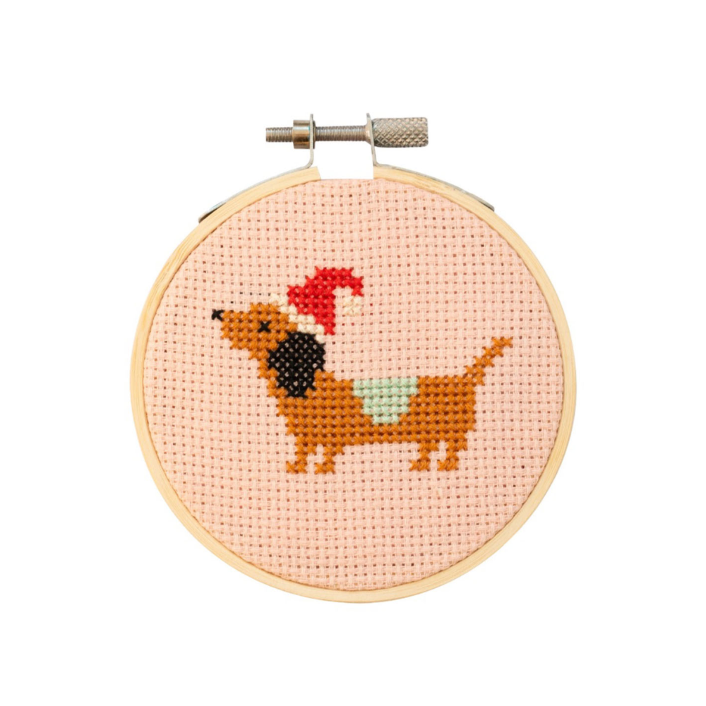 Cross-stitched dachshund with a red bow tie in a wooden hoop on a white background