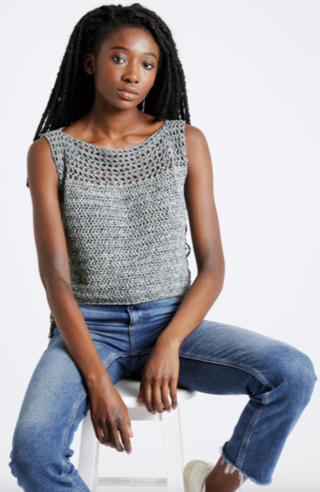 Woman with braids in a pair of jeans wearing a speckled crocheted top on a white background.