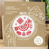 Embroidery kit packaging with red and white bird design on a brown background