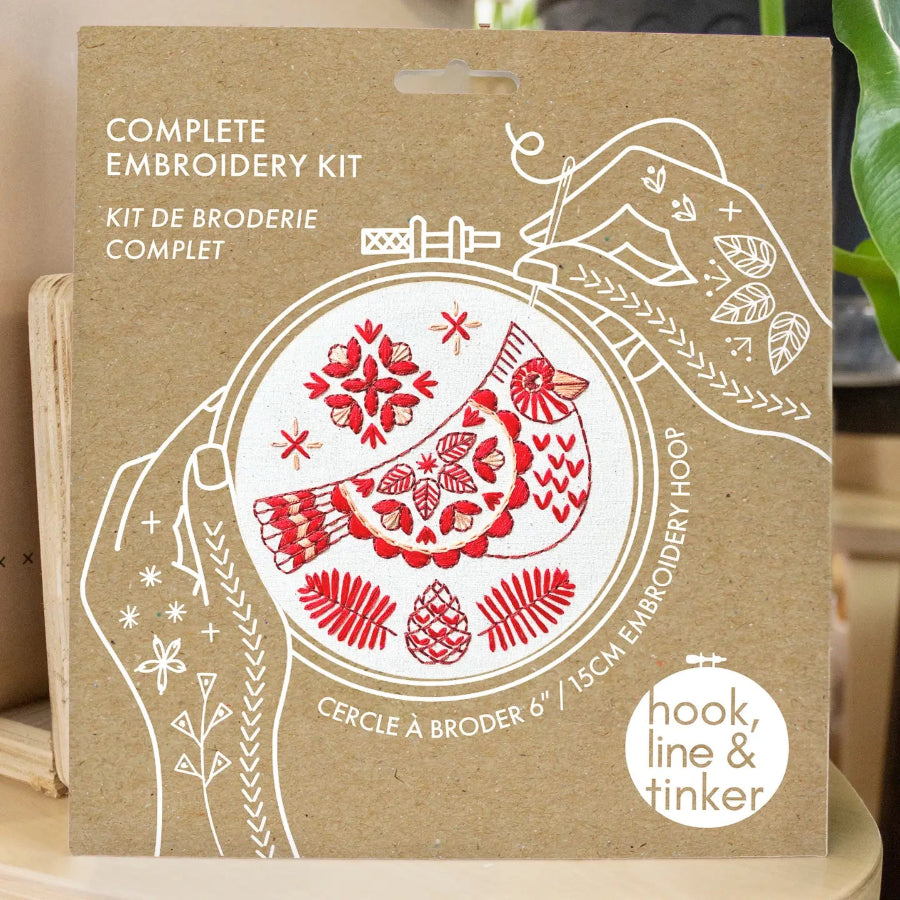Embroidery kit packaging with red and white bird design on a brown background