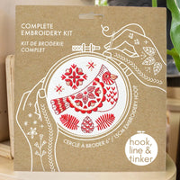 Embroidery kit packaging with red and white bird design on a brown background