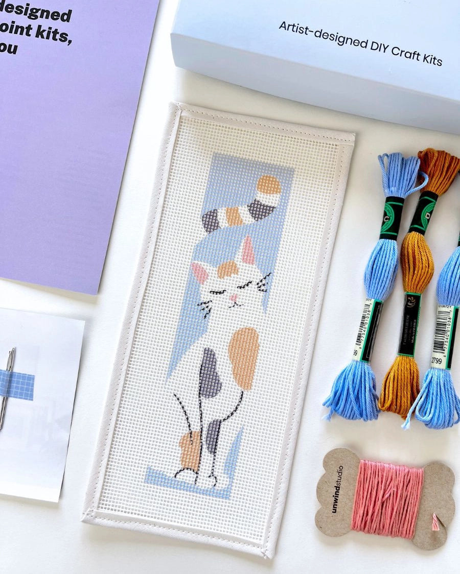 Needlepoint kit materials including a canvas and thread on a white background