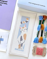 Needlepoint kit materials including a canvas and thread on a white background