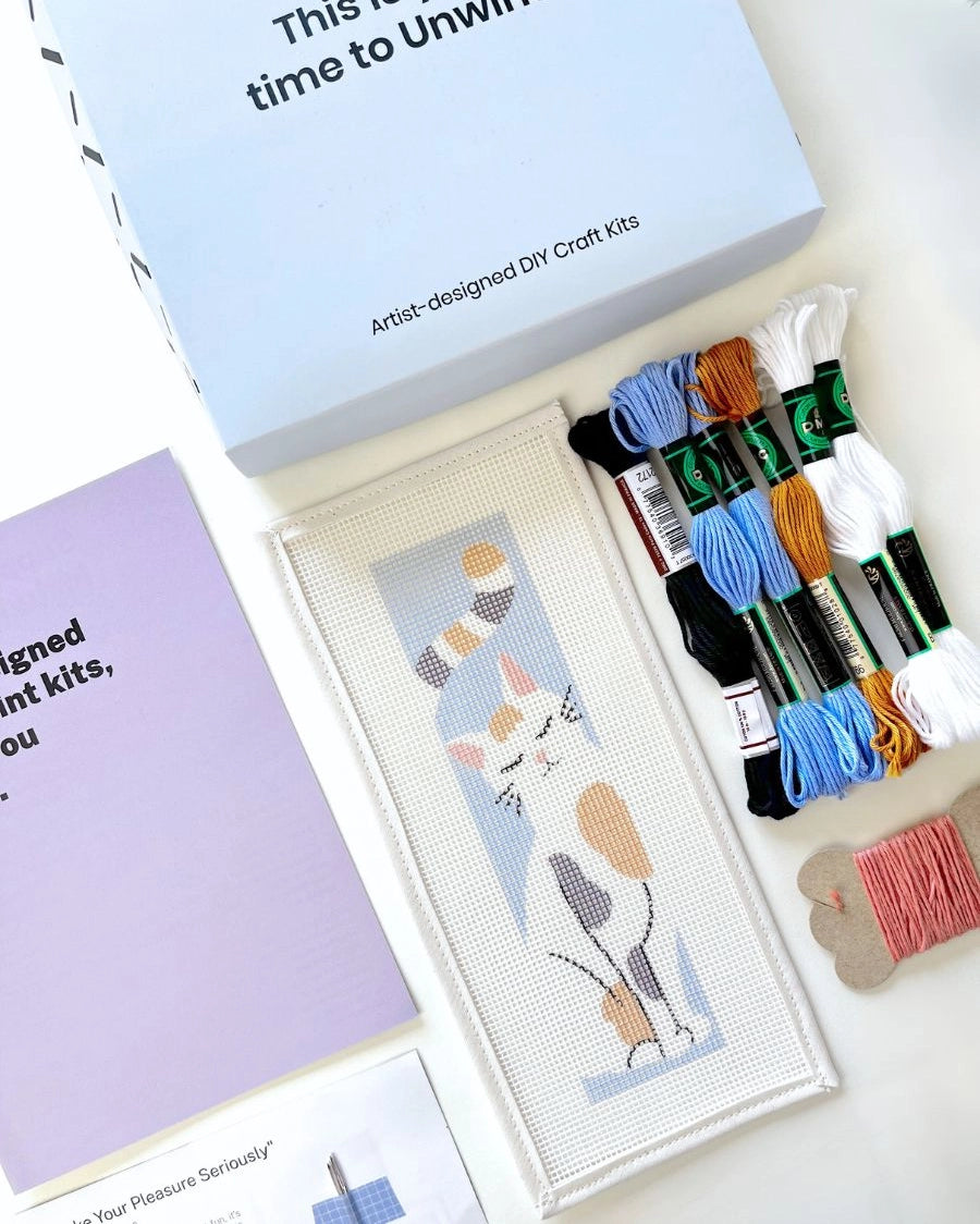 Needlepoint kit materials including a canvas and thread on a white background