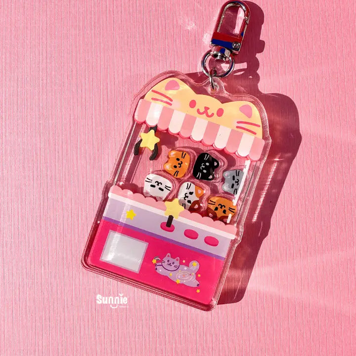 Cute pink claw machine keychain with small cat figures on a pink background