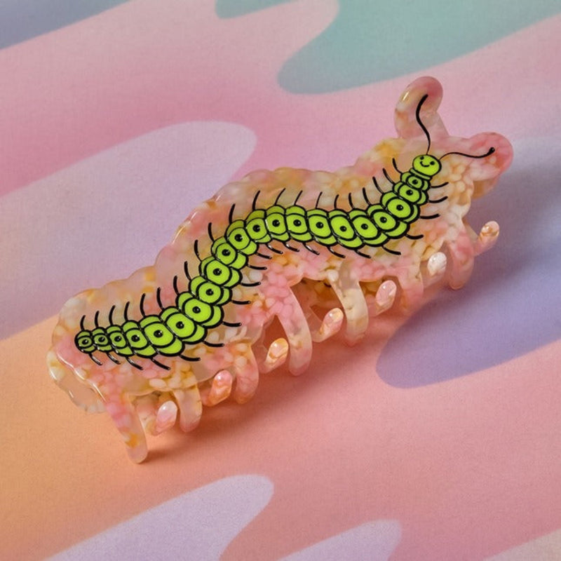 Pink and green caterpillar-shaped hair clip on a colorful background