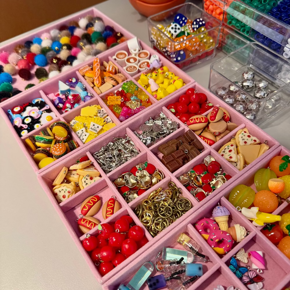 Assorted jewelry charms in a pink organizer on a table.