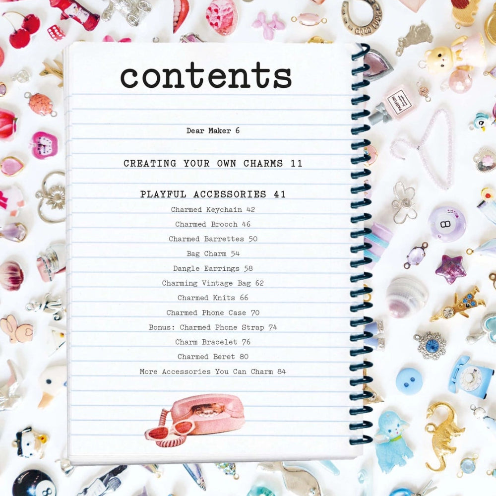 An open spiral-bound notebook showing a printed contents page surrounded by many pastel charms on a white background.