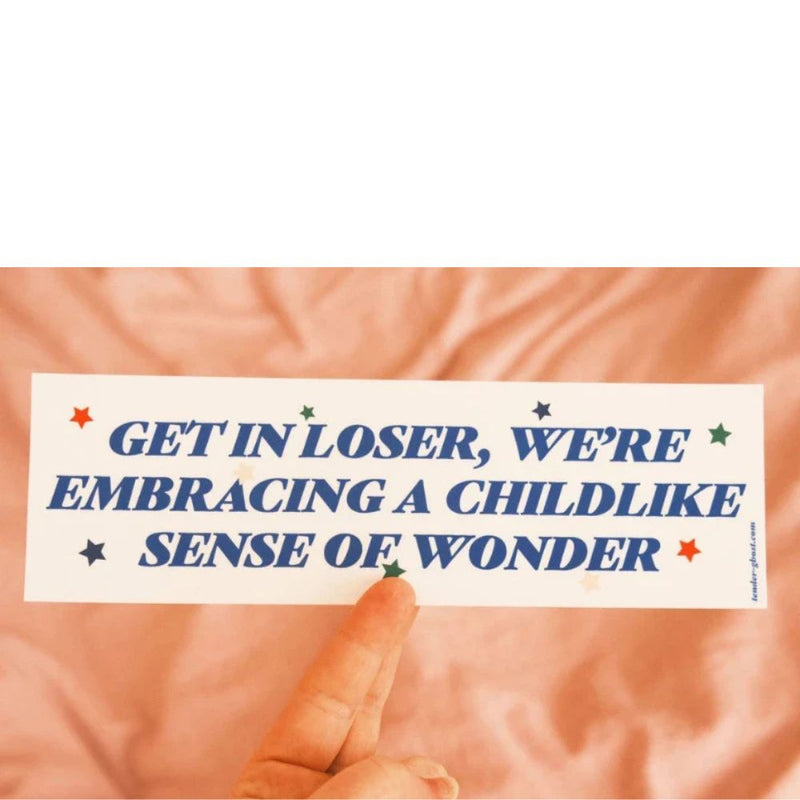 Text overlay " Get in loser we're embracing a childlike sense of wonder" on a textured peach background with a hand pointing to it.