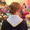 Woman facing a wall of yarn, wearing a crochet bandana on her back.