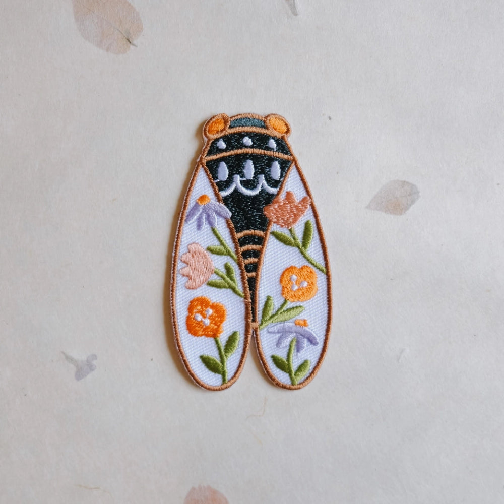 Decorative cicada-shaped patch with floral designs on a light background