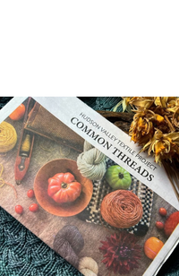 Newspaper with heading "Hudson Valley Textile Project Common Threads" and photo of pumpkins and various textile tools on a background of  a blue knit tablecloth with dried yellow flowers.