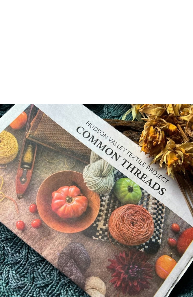 Newspaper with heading "Hudson Valley Textile Project Common Threads" and photo of pumpkins and various textile tools on a background of  a blue knit tablecloth with dried yellow flowers.