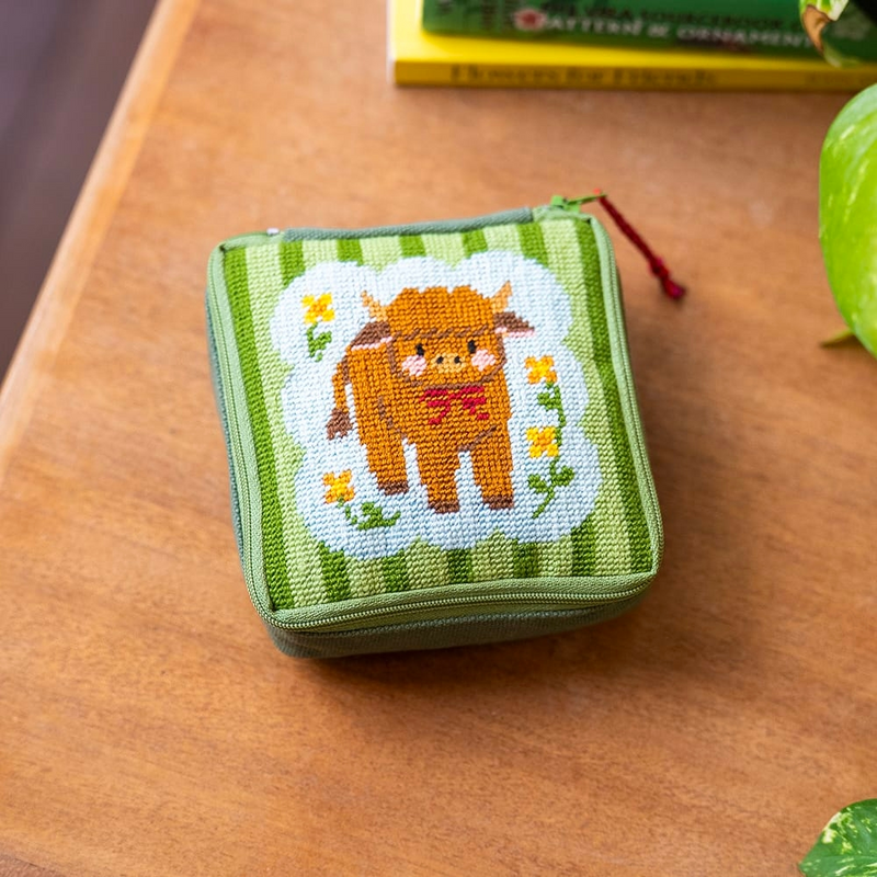A square zipper pouch with a needlepoint design featuring a highland cow on a green striped background