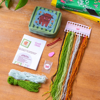 The kit for the needlepoint pouch showing all the included materials like colorful yarn, a needle, pre-sewn pouch and instructions