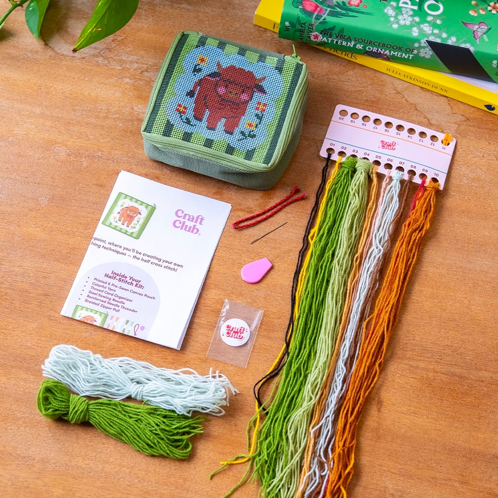 The kit for the needlepoint pouch showing all the included materials like colorful yarn, a needle, pre-sewn pouch and instructions