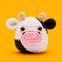 Crocheted cow toy with a pink nose on an orange background
