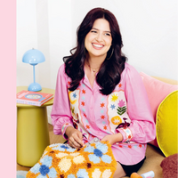 The author of Craft Club Yarn pictured seated on a couch working on a latch hook project from her book