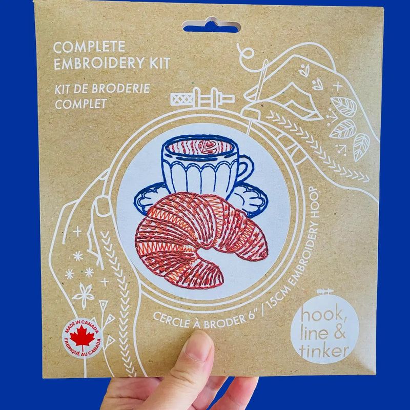 Embroidery kit packaging with a hand holding it against a blue background