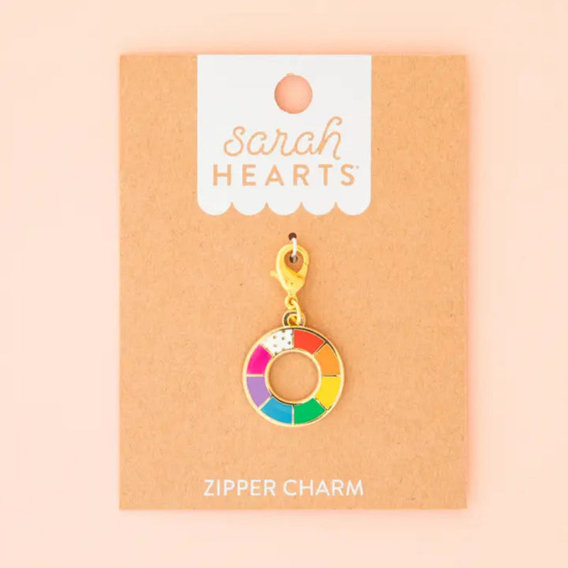 A zipper charm featuring a color wheel on Sarah Hearts packaging against a pink background.