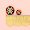 Pair of tortoiseshell patterned earrings with a ruler for scale on a pink background