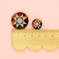 Pair of tortoiseshell patterned earrings with a ruler for scale on a pink background