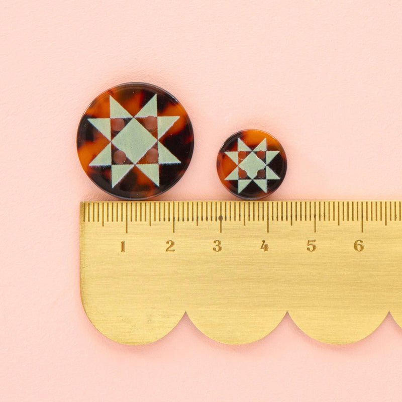 Pair of tortoiseshell patterned earrings with a ruler for scale on a pink background