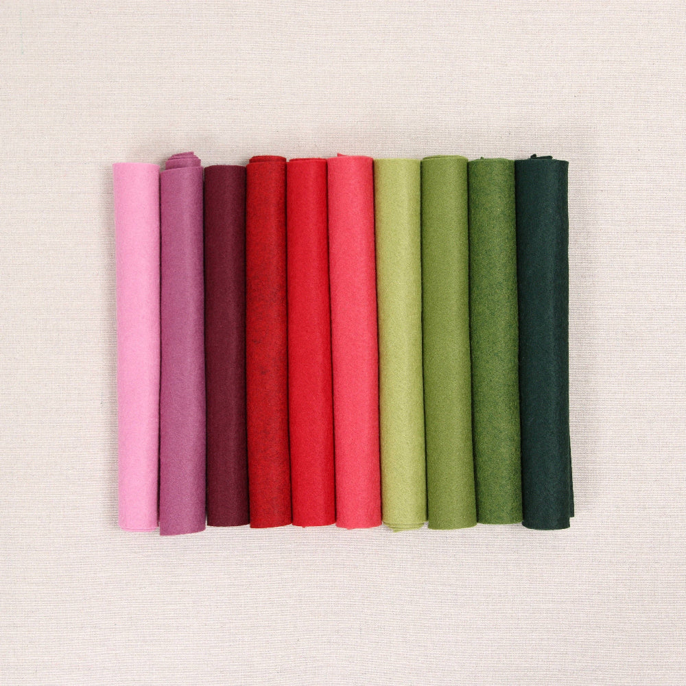 Various shades of felt sheet rolls in pinks, reds, and greens on a textured white background