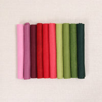 Various shades of felt sheet rolls in pinks, reds, and greens on a textured white background