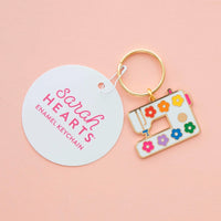 Colorful sewing machine keychain with 'Sarah Hearts' tag on a pink background