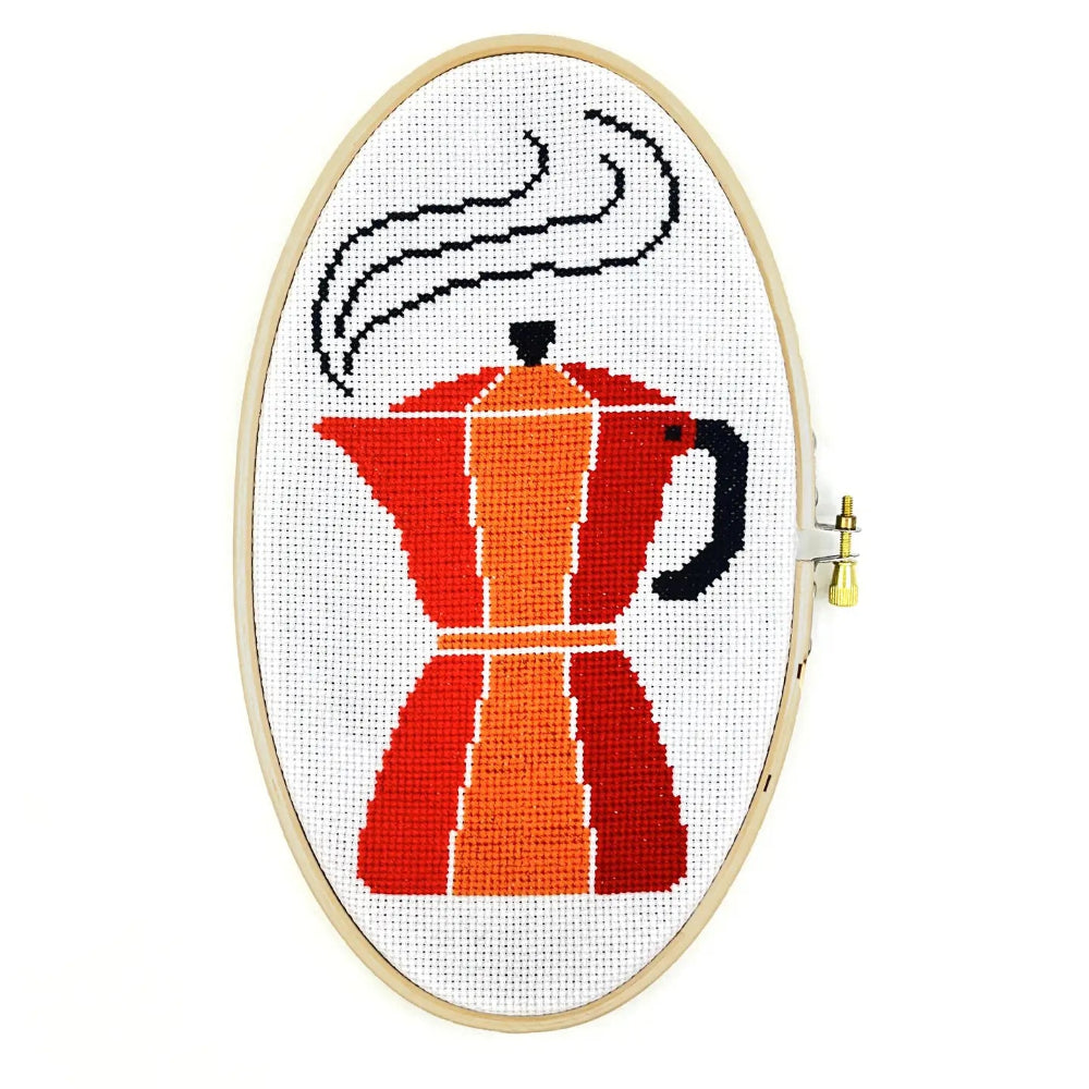 Cross-stitched design of a coffee maker in an embroidery hoop on a white background