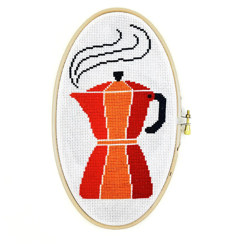 Cross-stitched design of a coffee maker in an embroidery hoop on a white background
