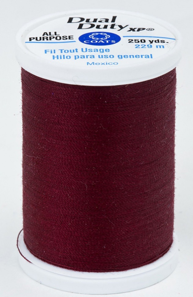 A spool of dark red Dual Duty XP sewing thread with a white label featuring blue and black text, set against a plain white background.