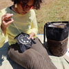 Person sitting outdoors with a black bag and a small black device on a green blanket.