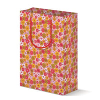 Floral patterned gift bag with red handles on a white background