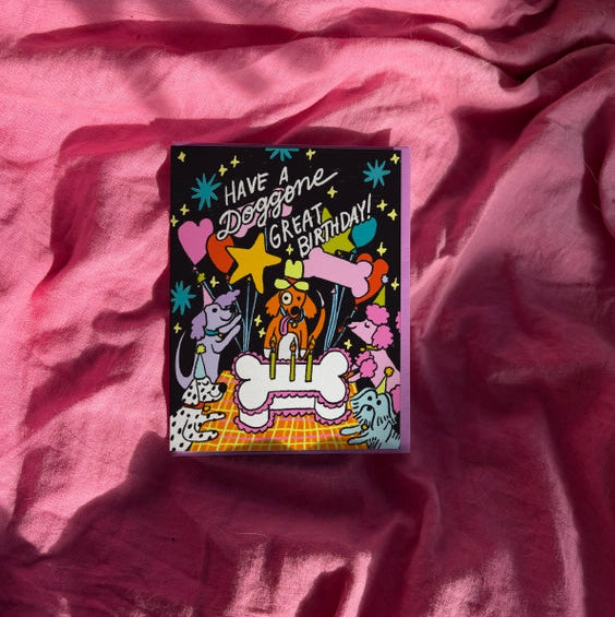 Black card with dogs eating bone shaped cake. 'Have a doggone great birthday'