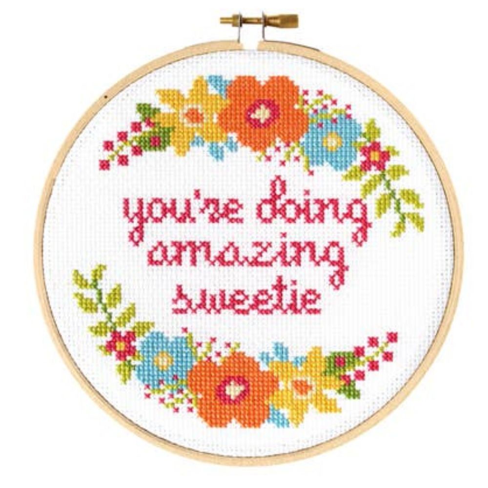 Cross-stitched hoop with colorful flowers and text 'you're doing amazing sweetie' on a white background