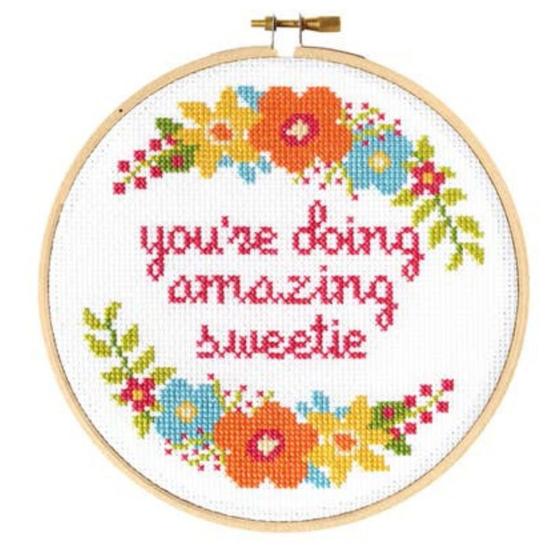 Cross-stitched hoop with colorful flowers and text 'you're doing amazing sweetie' on a white background