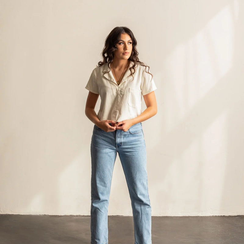 A woman wearing a white collard shirt and blue jeans.