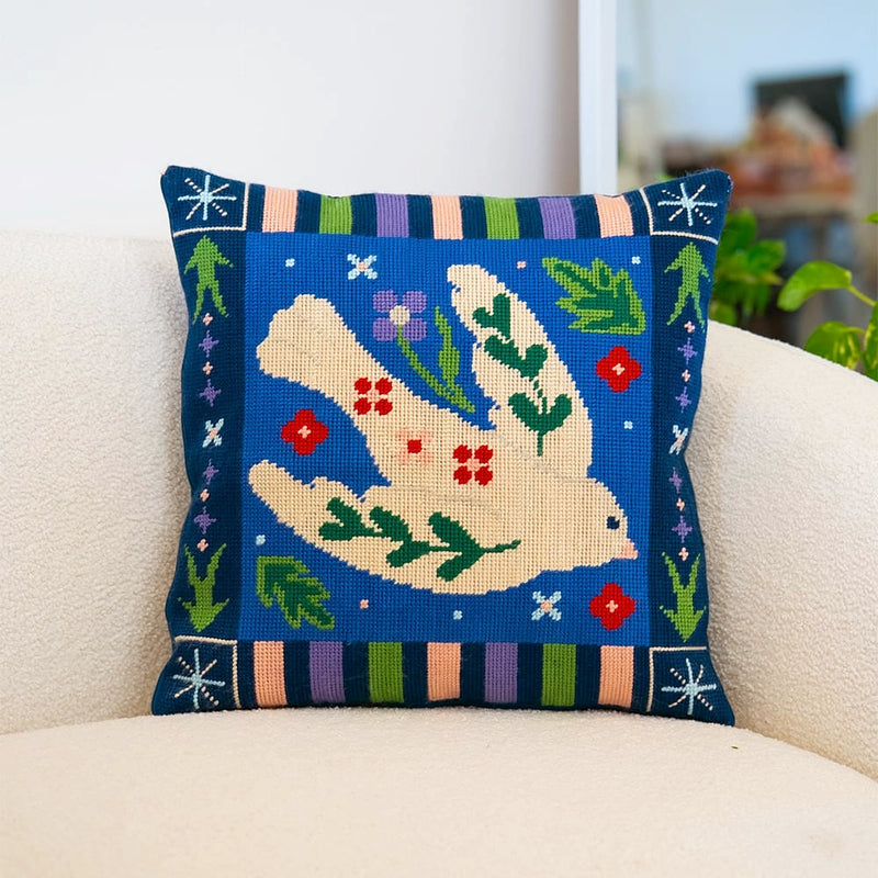 A needlepoint cushion with a blue floral design featuring a white dove in the middle of a blue background.
