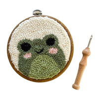 Embroidery hoop with a green and white face design and a wooden needle on a white background