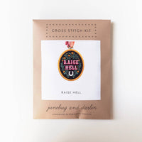 Cross stitch kit packaging with 'Raise Hell' design on a white background