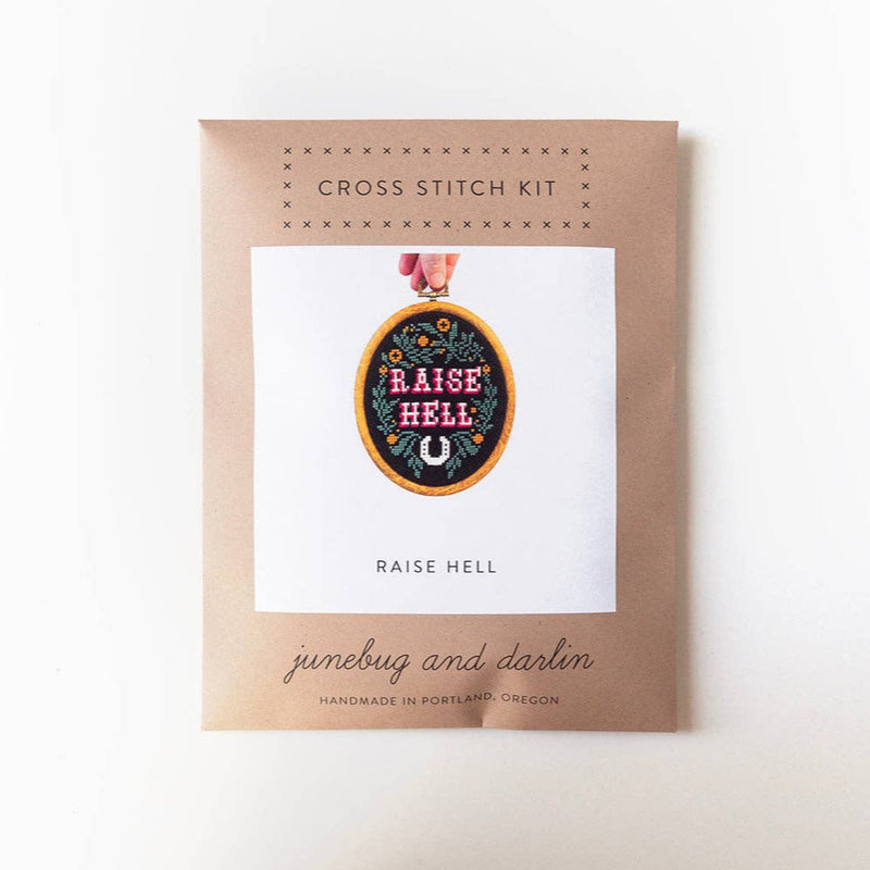 Cross stitch kit packaging with 'Raise Hell' design on a white background