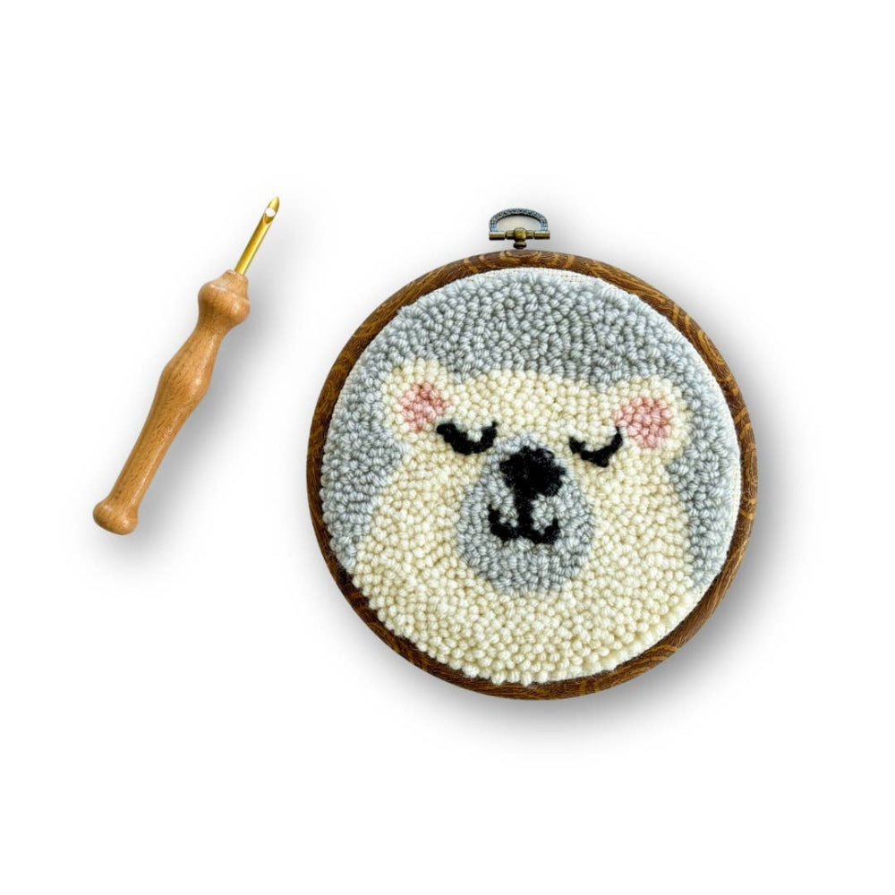 Embroidery hoop with a sleeping bear design and a crochet hook on a white background