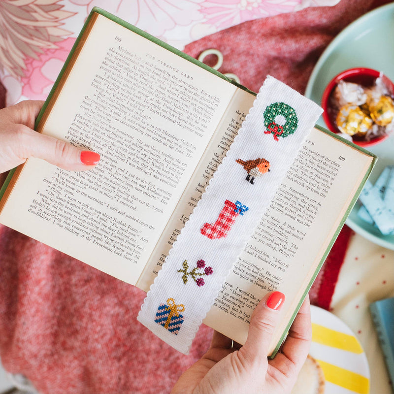 Person holding a book with a cross-stitched bookmark featuring Christmas designs.
