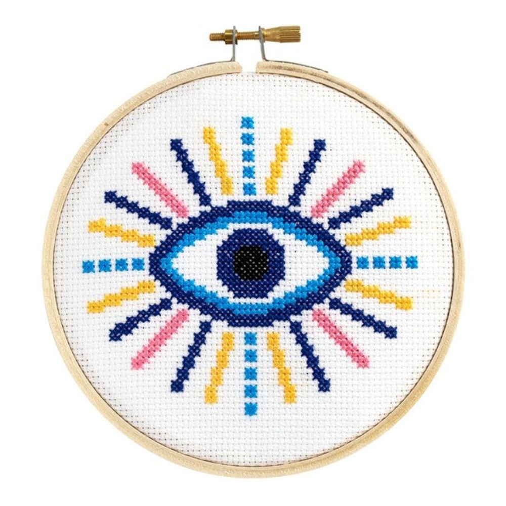 Cross-stitched eye design in a wooden hoop on a white background
