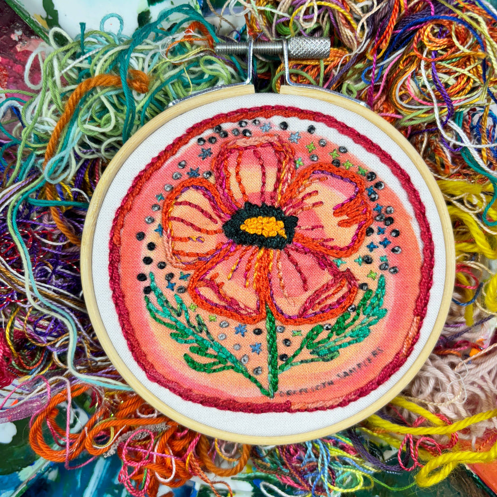 Embroidery hoop with a colorful floral design surrounded by various threads.