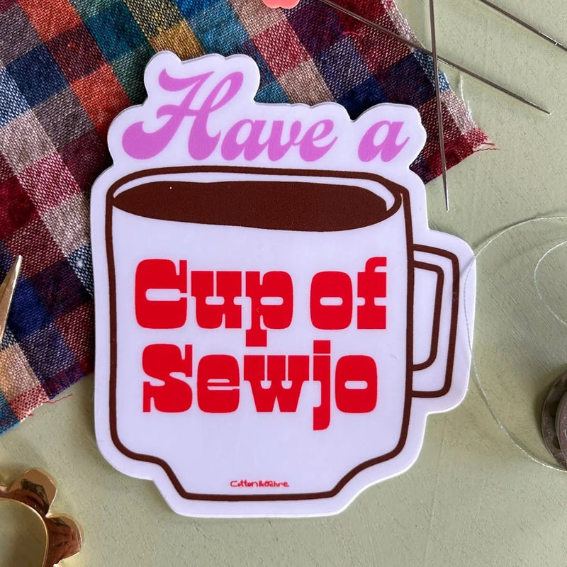 Sticker in the shape of a cup of coffee with "Have a cup of sewjo" printed in pink and red on it